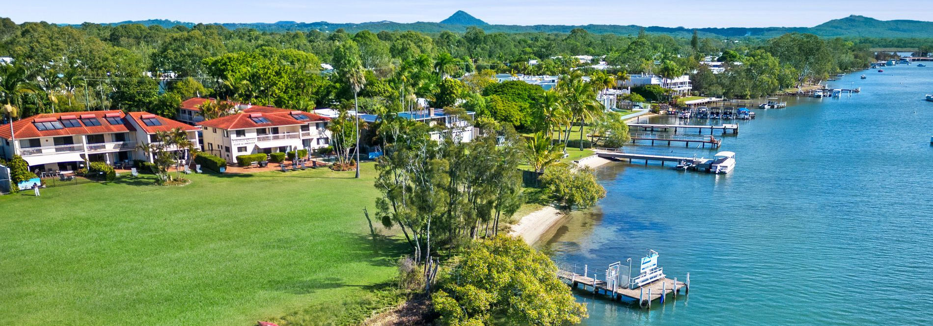 Aerial view of Cayman Quays and the beautiful Noosa River Aerial view of Cayman Quays Noosaville holiday property highlighting the private jetty, resort facade, expansive Noosa River, and distant hinterland.