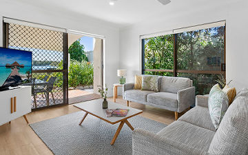 4-Bedroom Townhouse Living Zone and Fenced Courtyard Spacious multi-level 4-bedroom holiday townhouse at Cayman Quays highlighting an expansive family lounge with sliding doors opening onto a large private patio courtyard with direct Noosa River views.