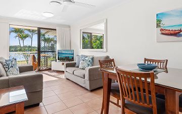 Riverside Apartment Lounge Room and Private Patio Riverside Apartment lounge area at Cayman Quays Noosaville, showcasing a large TV, dining furniture, and glass sliders transitioning out to a private patio with Noosa River views.